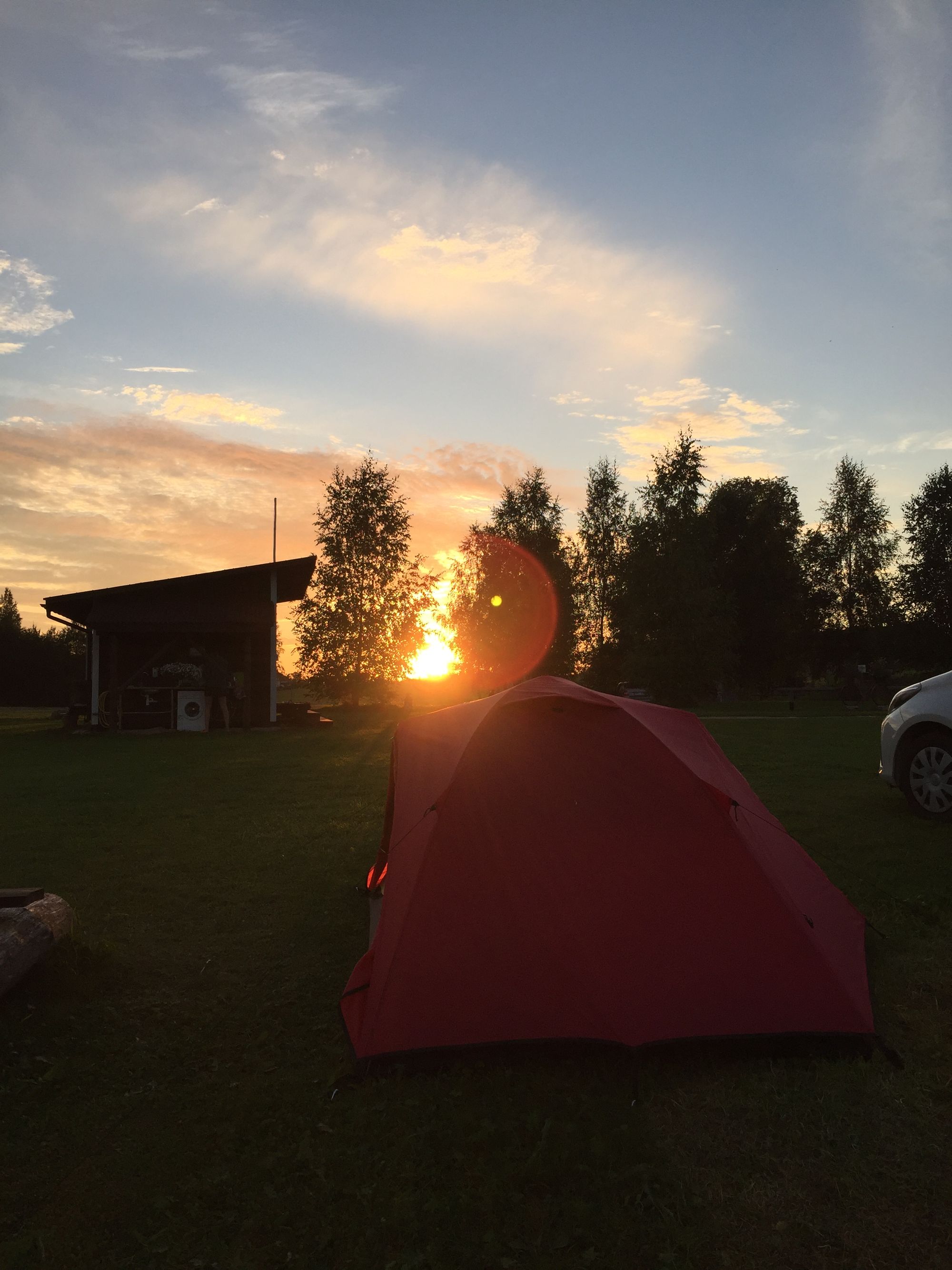 Die Sonne geht unter hinter den Huegeln und hinter dem roten Zelt
