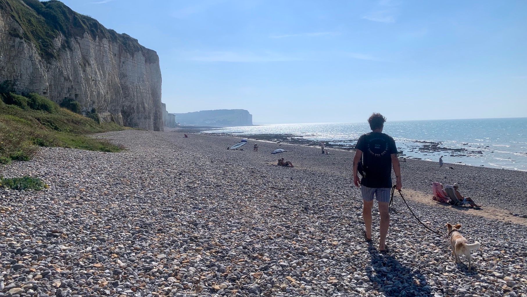 Mann geht mit Hund am Strand in der Normandie entlang.