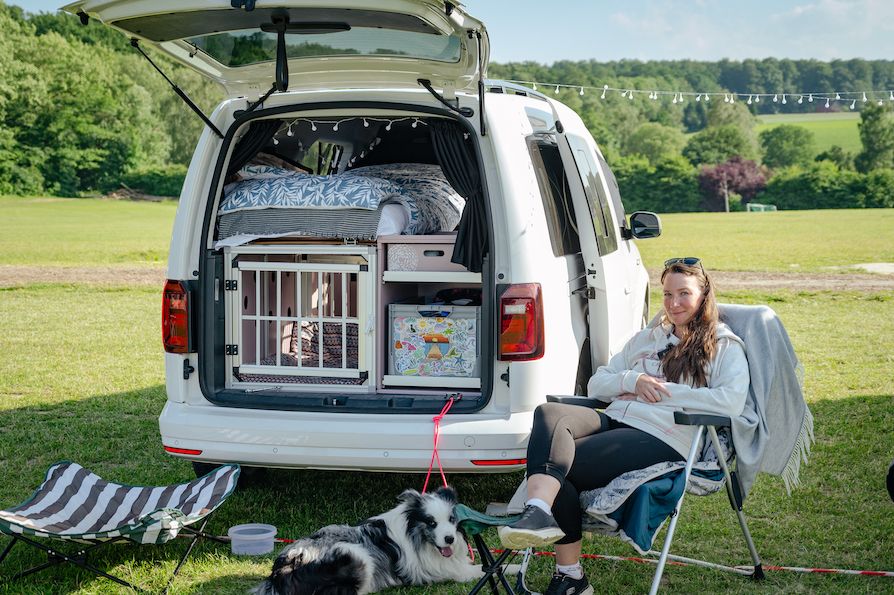 Frau sitzt mit ihrem Hund vor ihrem ausgebautem Caddy.