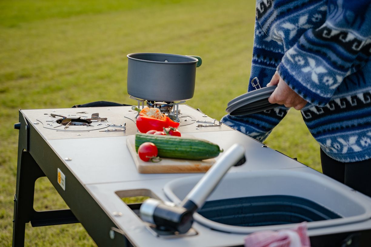 Nahaufnahme von einer mobilen Campingküche draußen, auf der Essen zubereitet wird.