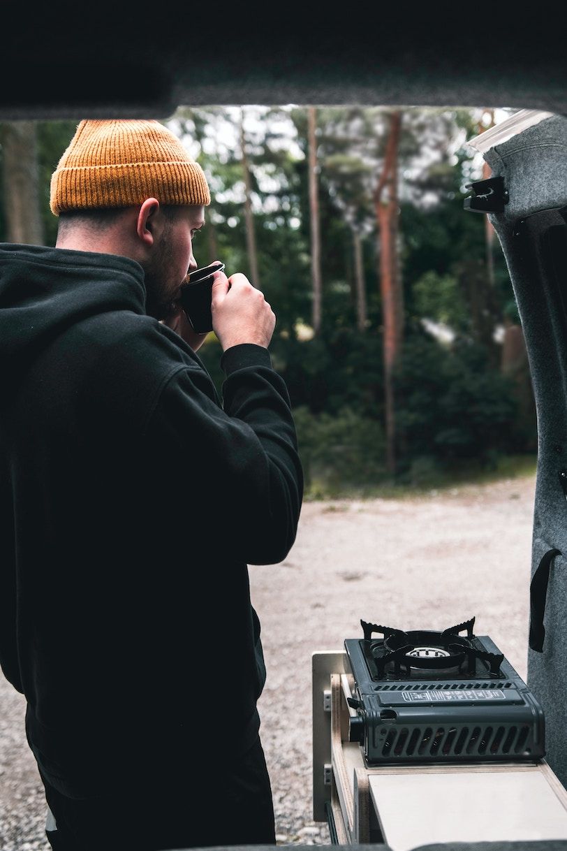 Mann trinkt Kaffee neben seiner Heckküche im Auto. 