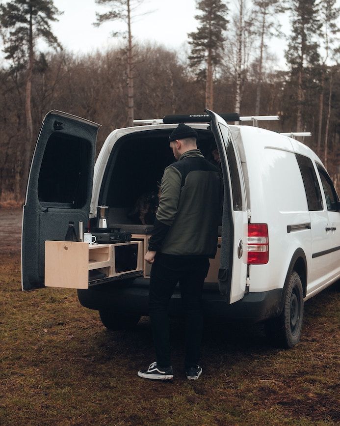 Mann steht an einer Campingbox am Kofferraum eines Caddys.