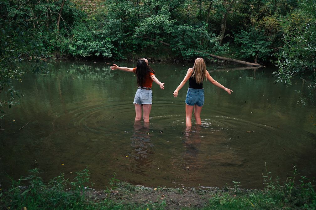 Zwei Mädchen stehen in kurzen Sommerhosen in einem Fluss.