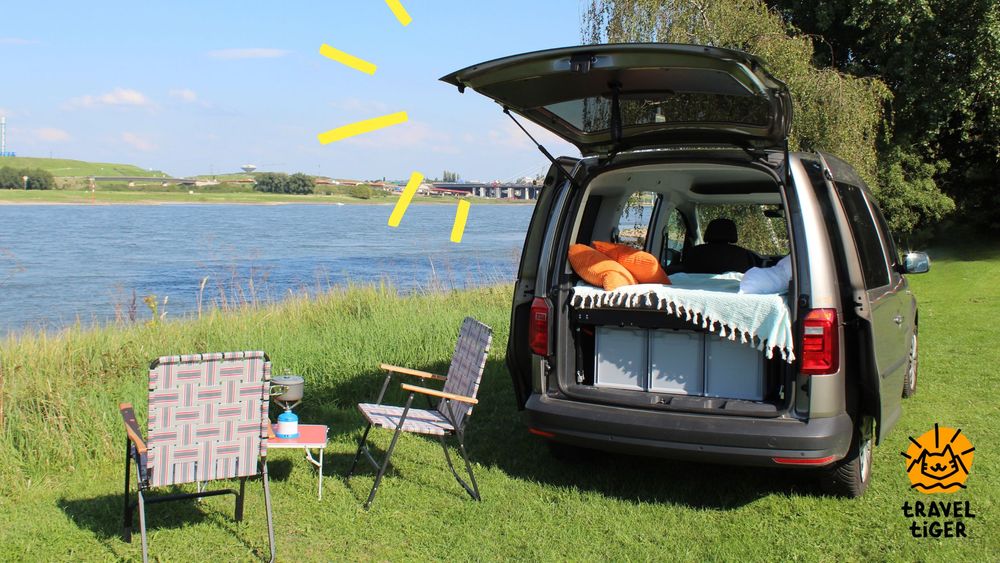 Camping mit dem Hochdachkombi: Ein VW Caddy steht mit Campingbett am Fluss. 
