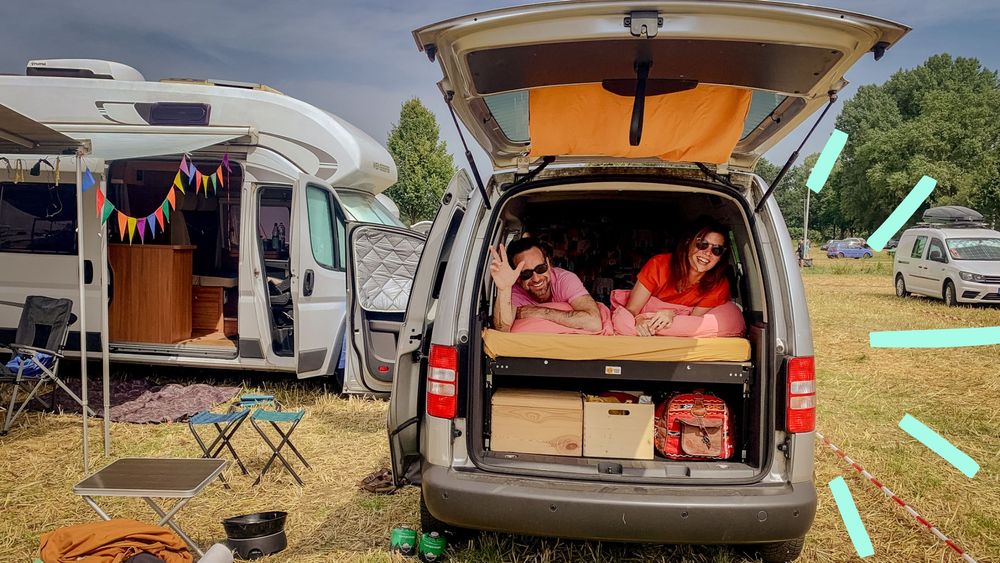 Ein Paar liegt glücklich in einem Minicamper auf einem Festivalgelände.