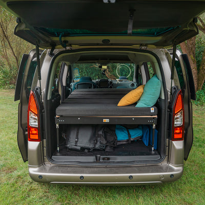 Photo of open tailgate and set up camping bed in the trunk.