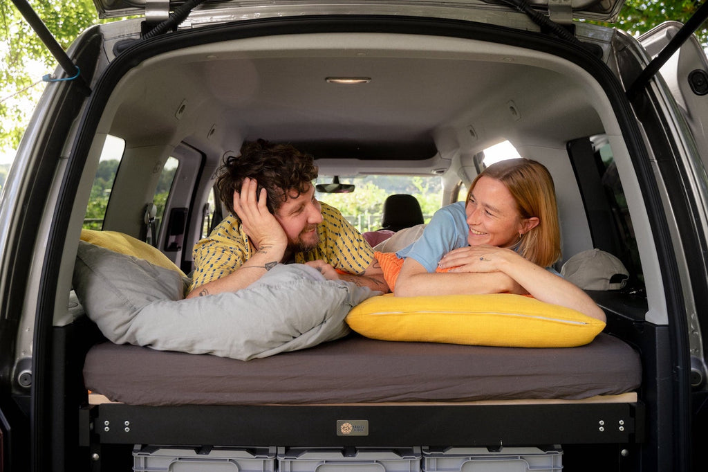 Paar liegt auf Campingbett mit Matratze fürs Auto. 