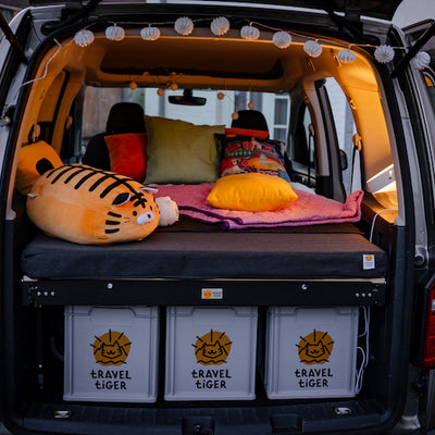 VW Caddy stands on a meadow with the trunk open and a camping bed.