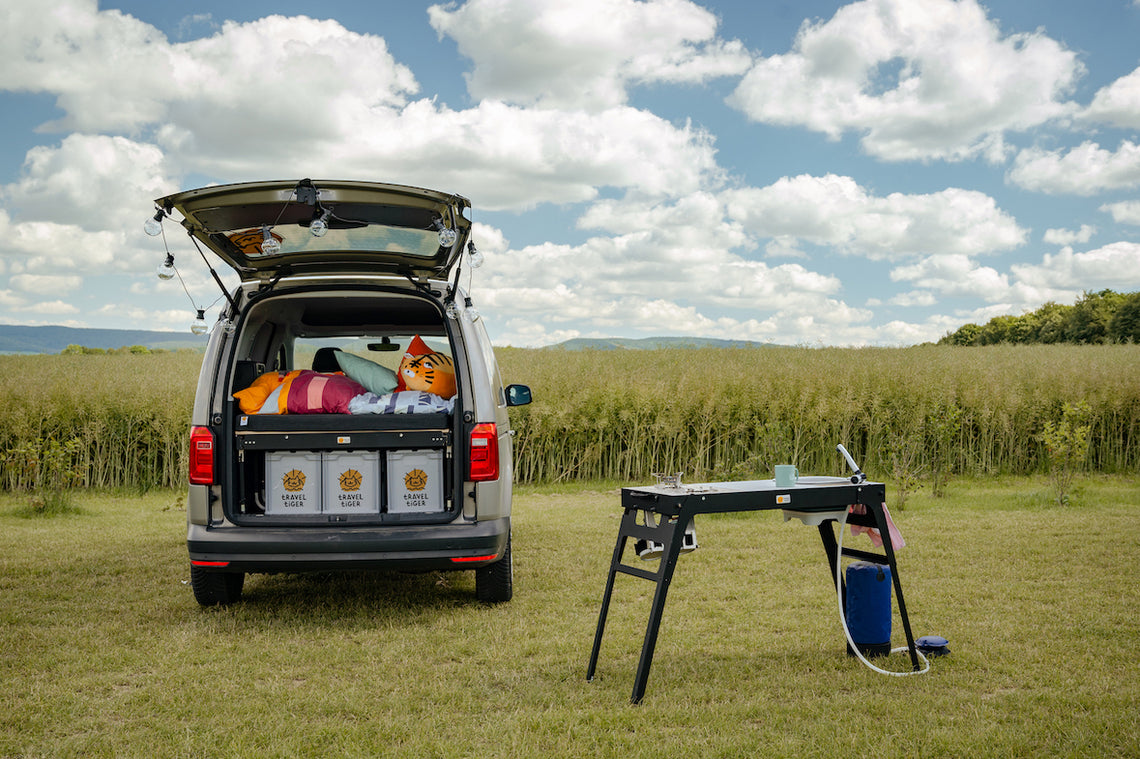 Moodbild von Minicamper mit mobiler Campingküche auf einer Wiese.